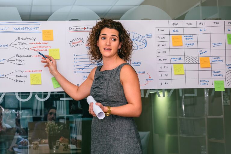 A woman with short hair points at words on a white sheet of paper on the wall