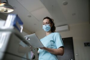 A woman wears scrubs and a face mask while checking information