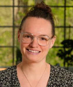 A woman with glasses and a black shirt smiling.
