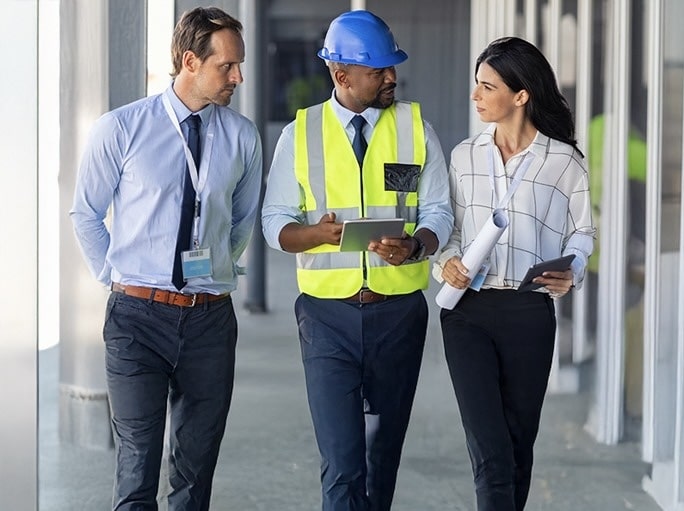 Three people in hard hats walking down a hallway.