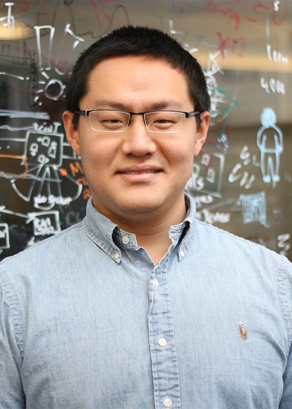 A man with dark hair and glasses, wearing a light-colored button-down shirt