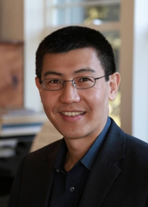 A man with dark hair and small glasses smiles in a headshot